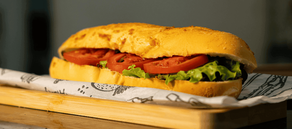 Baguete de parmesão com pate   tomate e alface em cima de uma tabua.
